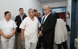 Isaías Fretes en bata blanca y Bachi Núñez en traje oscuro conversan, mientras una enfermera sonríe al fondo en un hospital.