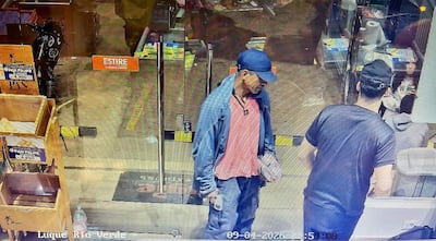 Hombre en camiseta roja y abrigo azul con paquete en mano, mientras otro en camiseta oscura atiende en mostrador.