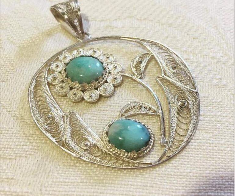 Colgante en plata con diseño floral, adornado con piedras azules, sobre fondo textil neutro.