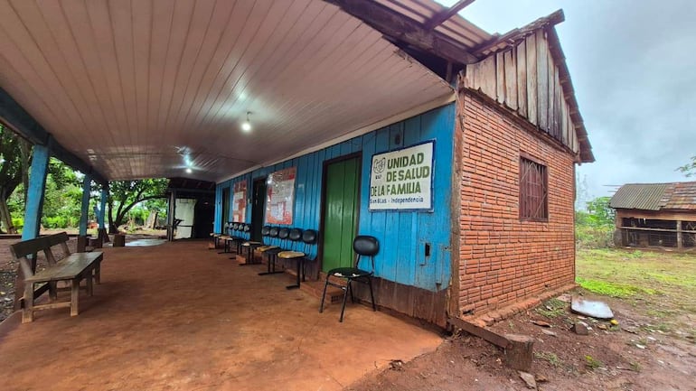 Unidad de salud rural con paredes azules y letrero visible, rodeada de vegetación y bancas de madera.