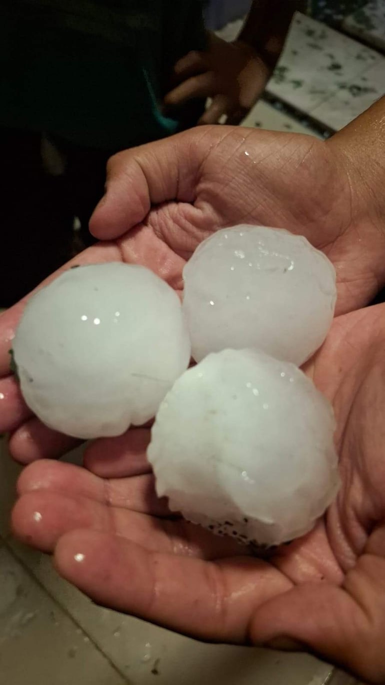 Dos manos de adulto sosteniendo tres bolas de granizo blancas y translúcidas con fondo de otras manos difusas.