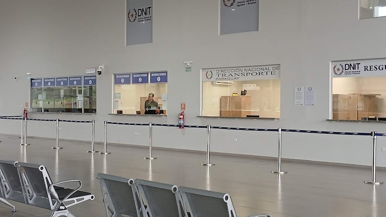 Amplio interior de oficina en la Dirección Nacional de Transporte, con ventanillas etiquetadas y asientos metálicos vacíos.
