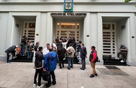 Periodistas observan desde la entrada de la sede de la Asociación del Fútbol Argentino (AFA), donde la Policía Federal realiza un allanamiento.