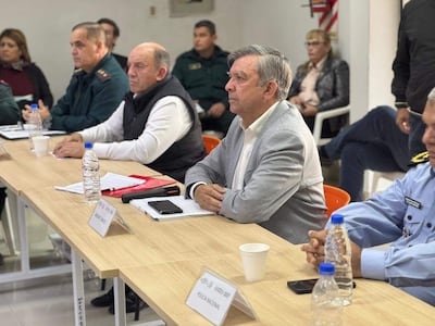 Seis personas, incluyendo funcionarios en uniforme, se reúnen alrededor de una mesa con documentos y botellas de agua.