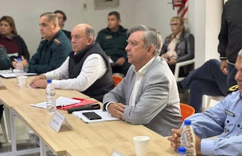 Seis personas, incluyendo funcionarios en uniforme, se reúnen alrededor de una mesa con documentos y botellas de agua.