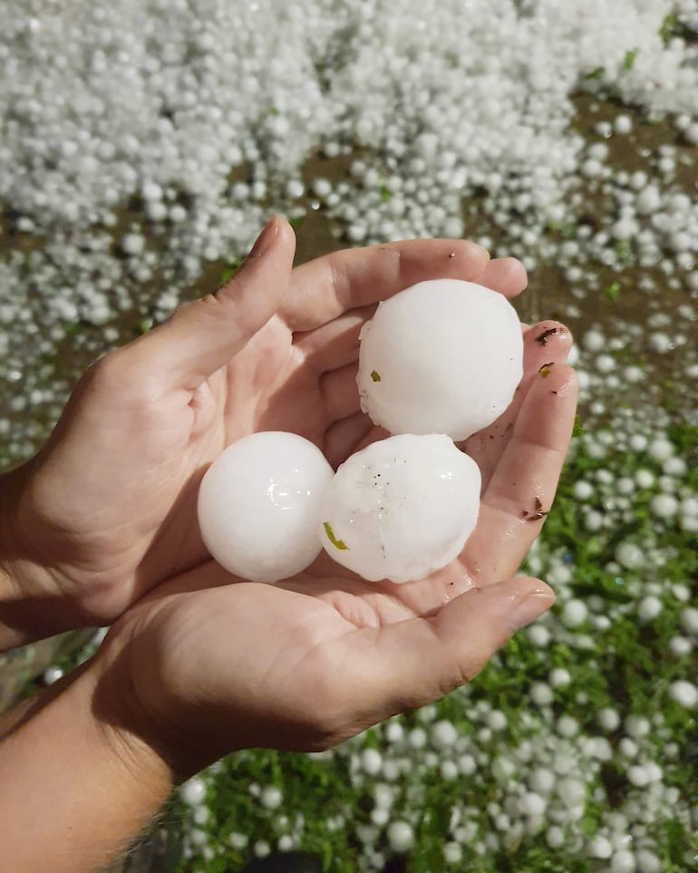 Manos sosteniendo grandes bolas de granizo sobre un terreno cubierto, iluminado en condiciones nocturnas.