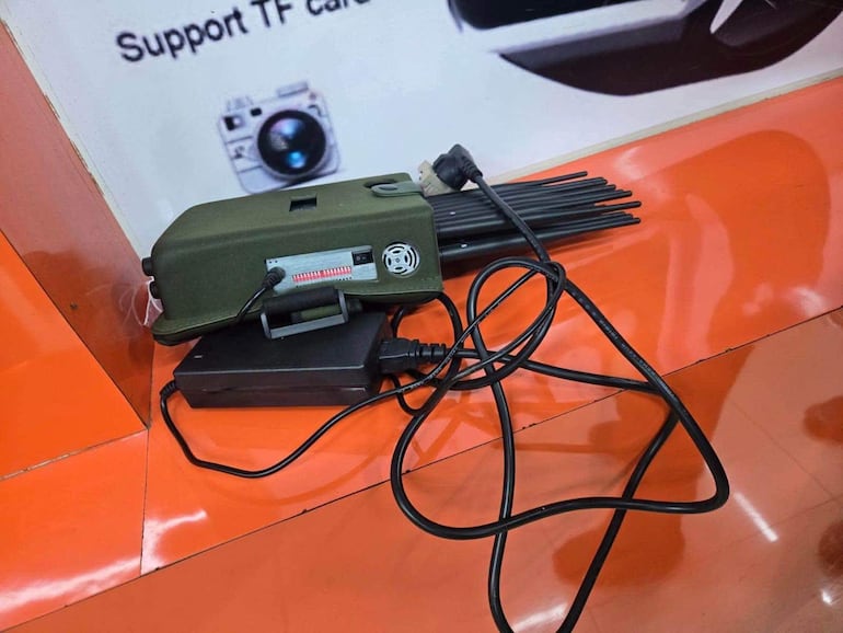 Dispositivo técnico verde sobre superficie naranja, rodeado de cables en un ambiente interior.