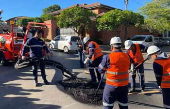 Luis Fernando Bernal junto a trabajadores en chalecos naranjas y cascos, esparciendo asfalto en una calle soleada.