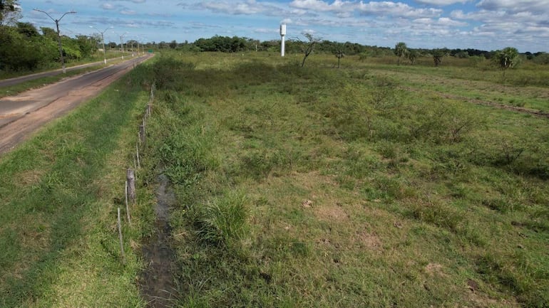 Paisaje rural con camino de tierra y tanque de agua elevado, rodeado de vegetación densa y cielos nublados.