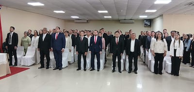 Grupo diversificado de 40 personas en trajes formales, con expresiones serias, en salón de eventos.