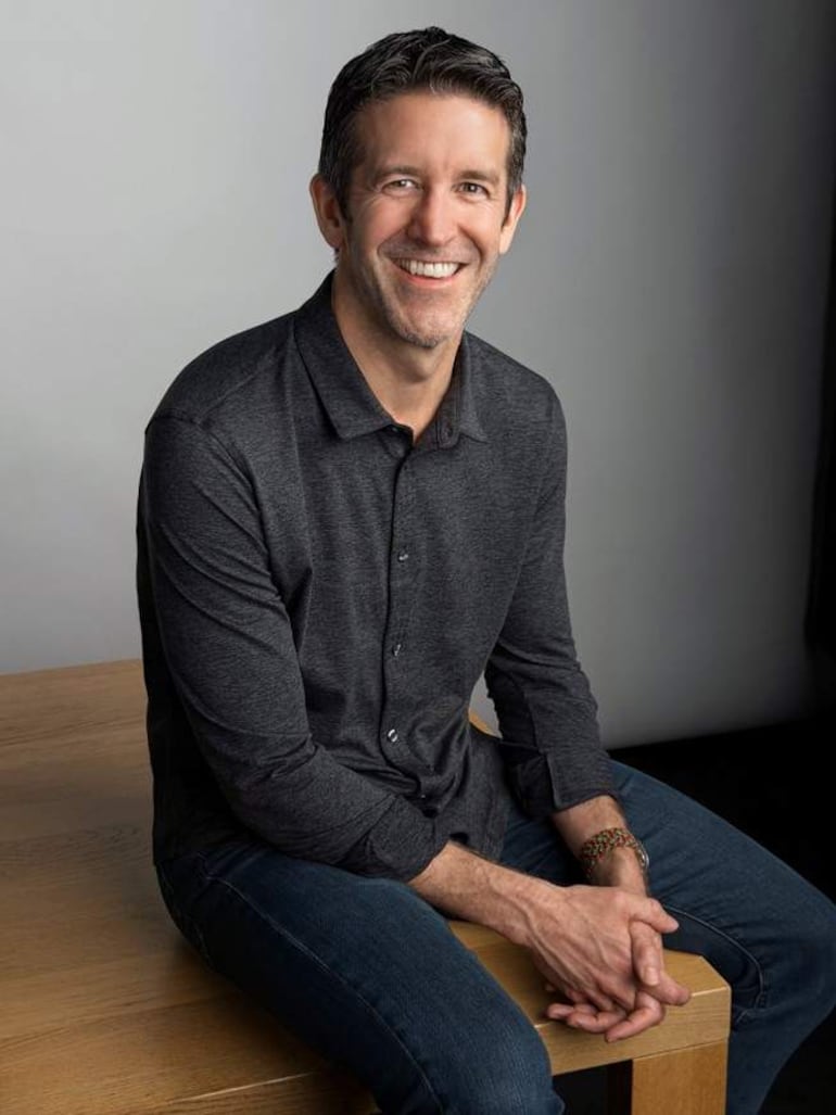 John Ternus y Tim Cook sonríen mientras están de pie en el escenario, con rostros alegres y gestos entusiastas.