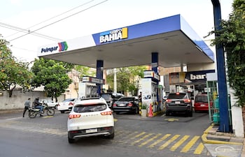 Situación en estación Petropar con autos en fila y motocicleta con conductor en casco, rodeados de árboles en un ambiente nublado.