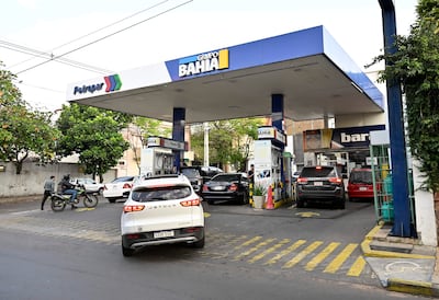 Situación en estación Petropar con autos en fila y motocicleta con conductor en casco, rodeados de árboles en un ambiente nublado.