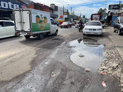 Escena urbana en la Avenida Santa Teresa con vehículos estacionados y un camión de jugo de naranja, charco y basura en la calle.