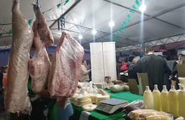 Personas en un mercado de alimentos, con carnes y productos lácteos expuestos sobre mesas bajo carpa.