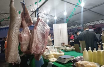 Personas en un mercado de alimentos, con carnes y productos lácteos expuestos sobre mesas bajo carpa.