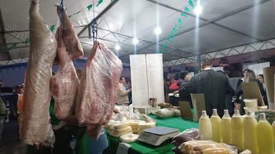 Personas en un mercado de alimentos, con carnes y productos lácteos expuestos sobre mesas bajo carpa.