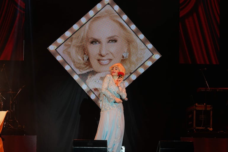 Fátima Flórez en un vestido brillante, sosteniendo una rosa, actuando con imagen de fondo de mujer sonriente.
