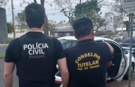 Dos hombres de espaldas, uno en chaleco de Policía Civil Paraná y otro de Consejo Tutelar, revisan un automóvil en la calle.