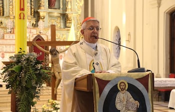 El cardenal Adalberto Martínez de pie en un altar con vestimenta blanca, hablando al público con fondo decorado por un crucifijo.
