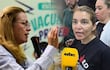 María Teresa Barán con camisa clara y gesticulando, y Rossana González en vestimenta oscura, hablando intensamente en un evento interior, con cartel de 'VACUNA' detrás.