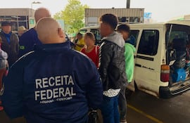 Funcionarios de Receita Federal supervisan a jóvenes en control aduanero, con chaquetas azules y ambiente de seguridad.