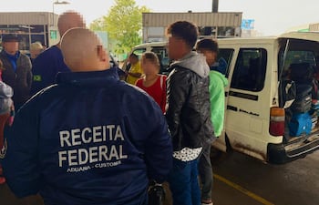 Funcionarios de Receita Federal supervisan a jóvenes en control aduanero, con chaquetas azules y ambiente de seguridad.