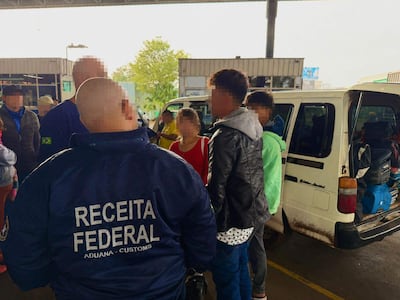 Funcionarios de Receita Federal supervisan a jóvenes en control aduanero, con chaquetas azules y ambiente de seguridad.