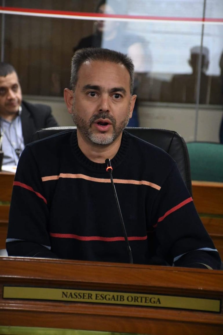 Nasser Esgai Ortega, con suéter oscuro con franjas rojas, blancas y azules, habla ante el micrófono en un ambiente institucional.