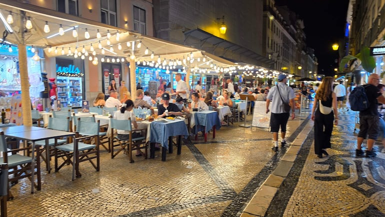 Restaurantes en Lisboa con mesas azules y gente conversando y riendo bajo luces colgantes.