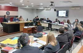 Cuatro peritos en mesa de reunión centrada en evidencias, con documentos y bandera paraguaya en fondo.