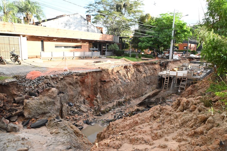Obra en construcción con terreno excavado, estructuras metálicas y motos estacionadas frente a un edificio de ladrillo.