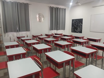 Aula vacía con escritorios blancos y sillas rojas, cortinas grises, y un mapa de países vecinos en la pared.