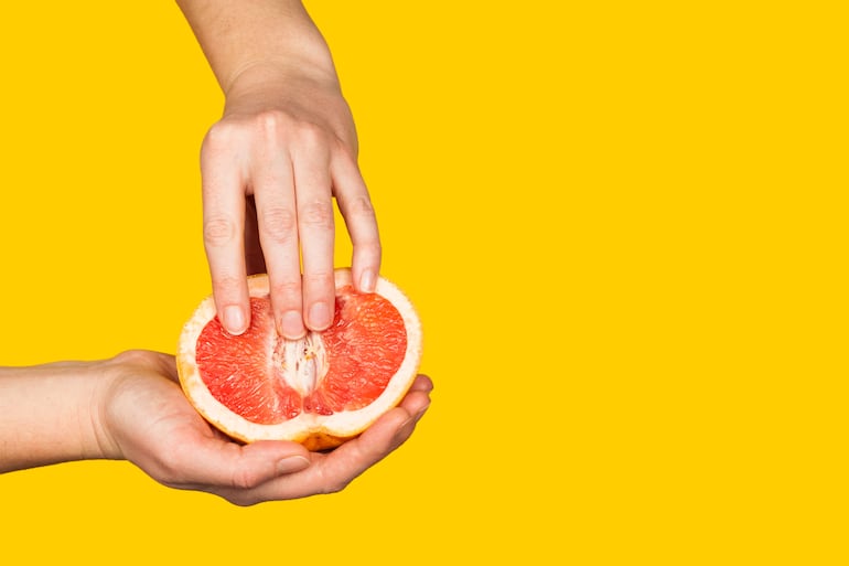 Dedos femeninos sobre un pomelo, concepto de vagina, clítoris, genitales.
