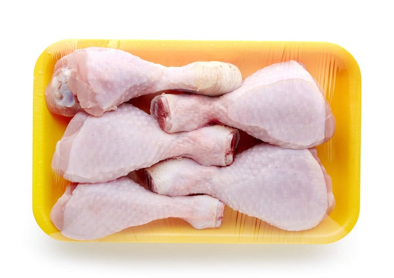 Muslos de pollo crudos apilados en envase amarillo, envueltos en plástico, en un entorno frigorífico.
