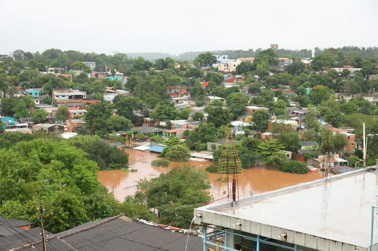 Paisaje urbano inundado en Ciudad del Este, con edificios y casas anegados por el agua, reflejando un ambiente de emergencia.