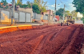 Escena de obra en la avenida Avelino Martínez, con máquina motoniveladora trabajando sobre terreno rojo sin personas visibles.