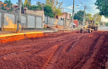 Escena de obra en la avenida Avelino Martínez, con máquina motoniveladora trabajando sobre terreno rojo sin personas visibles.
