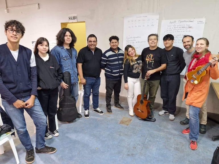 Diez personas en semicírculo, con mujer tocando ukulele y hombre con guitarra, en un aula con atmósfera de aprendizaje.