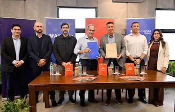 Jorge Mendelzon con saco negro y Santiago Lantermino calvo y atento, rodeados de hombres y una mujer en ambiente formal.