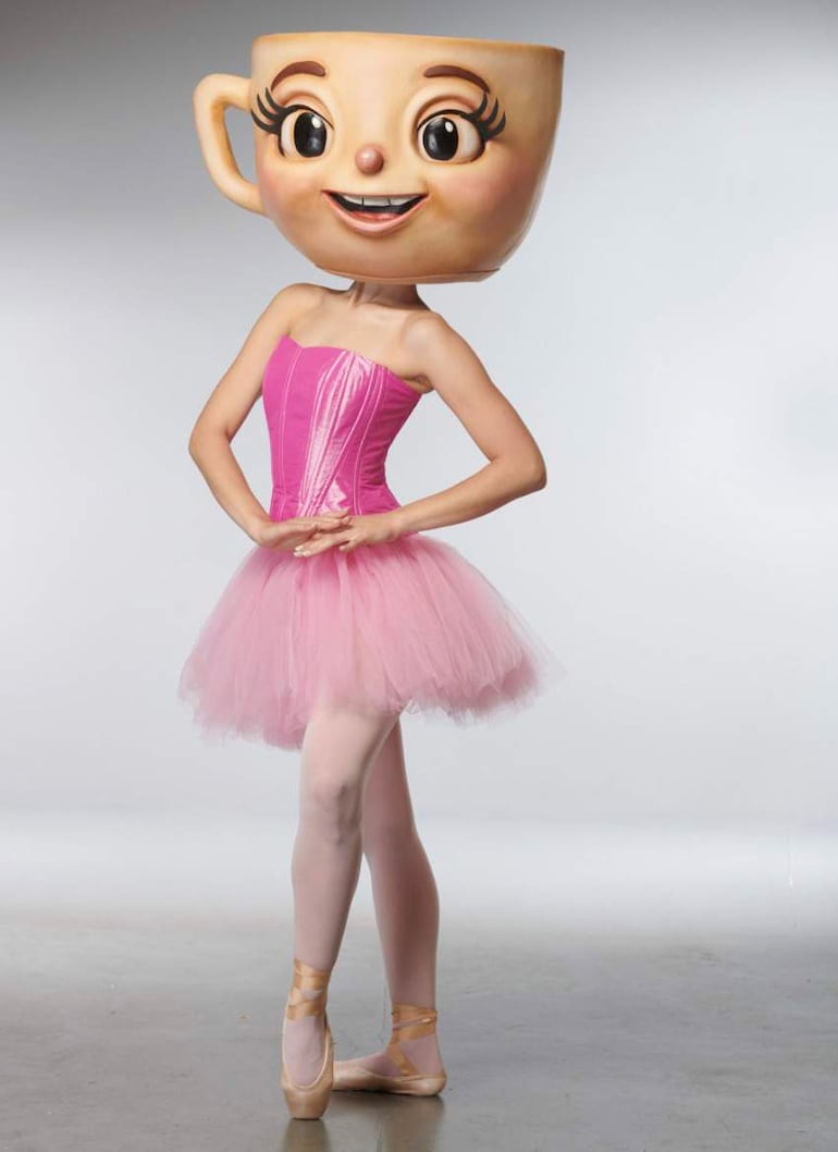 Intérprete disfrazada con cabeza de taza, posando en ballet en un fondo blanco, representando un espectáculo.