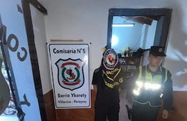 Hombre en camiseta negra y gorro junto a oficial de policía en uniforme en una comisaría.