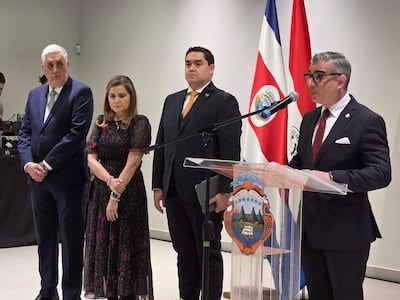 Jeison Granados en traje negro habla frente al atril, mientras Patricia Frutos y Miguel Aranda lo observan atentamente.