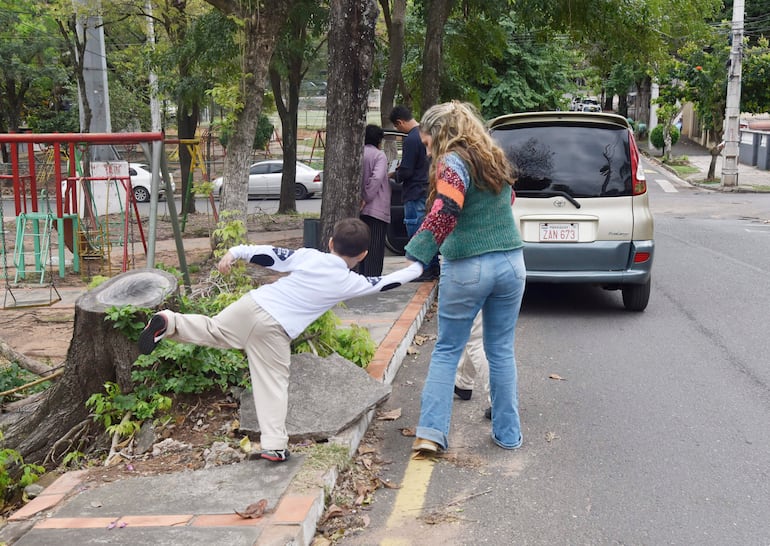 Niño vestido con camiseta blanca y pantalones claros, apoyado en una mujer con suéter colorido y jeans en un entorno urbano.