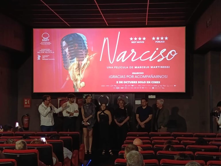 Belén Vierci sonríe junto a otros panelistas en elegante vestimenta, en una sala de cine decorada para el estreno de 'Narciso'.