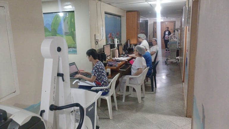 Seis profesionales de la salud en un ambiente hospitalario, con computadoras y equipo médico visible, mostrando concentración en su trabajo.