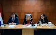 Mujer de cabello rubio con anteojos habla en mesa de juicio, mientras las otras dos personas la escuchan atentas.