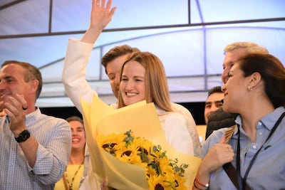 Soledad Núñez sonríe con un ramo de flores amarillas, acompañada de personas que aplauden y muestran alegría en un evento festivo.