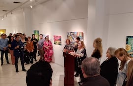 Mujeres de pie tras un podio en ceremonia, con expresiones de atención y ambiente artístico en la galería.