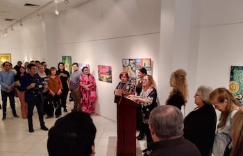 Mujeres de pie tras un podio en ceremonia, con expresiones de atención y ambiente artístico en la galería.